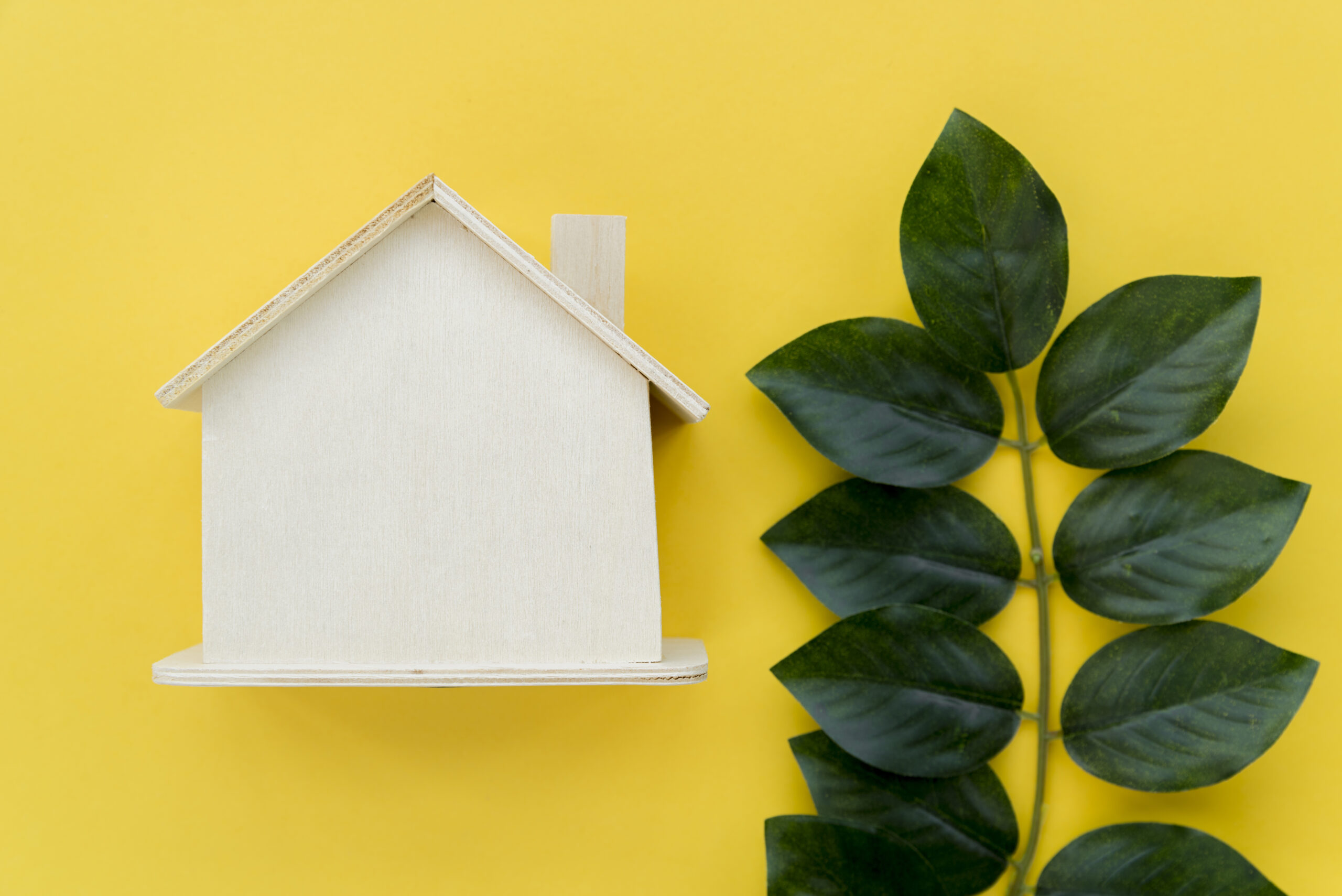 wooden-house-model-near-green-leaves-against-yellow-background